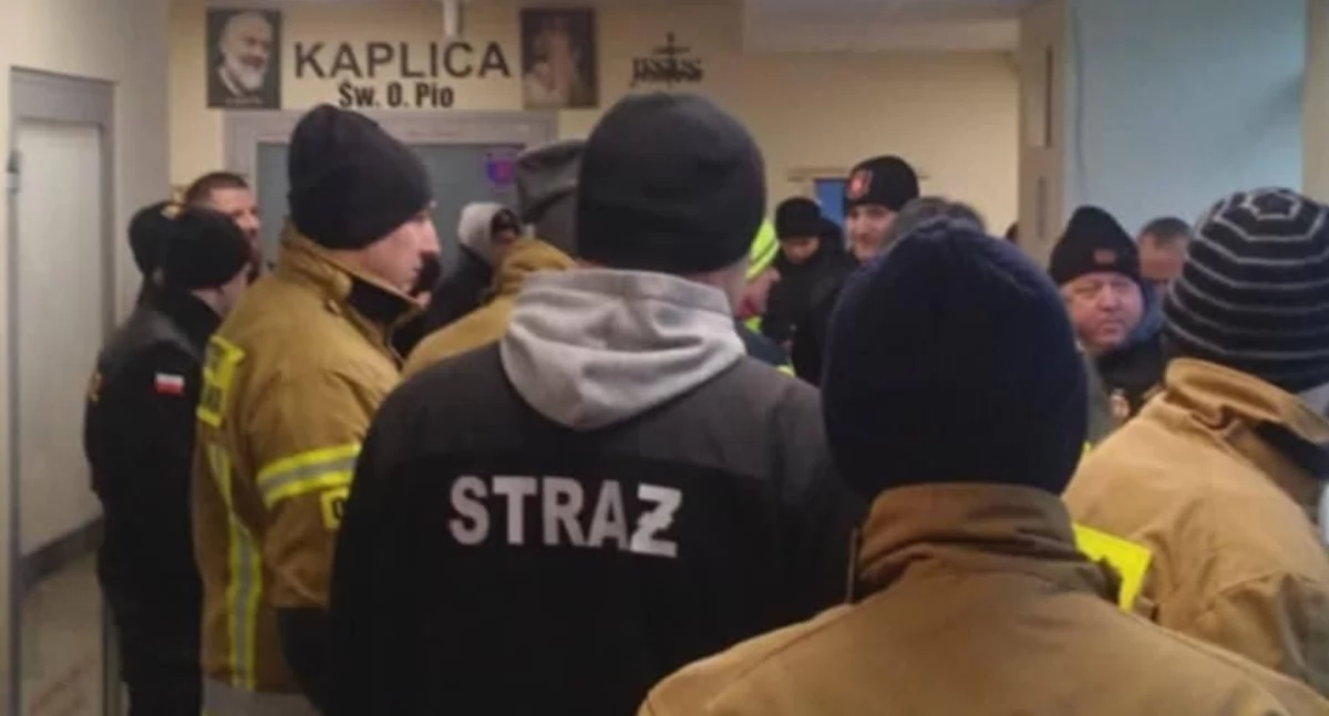 Strażacy OSP omawiają akcję przeniesienia łóżek medycznych w korytarzu szpitala w Sędziszowie Małopolskim.